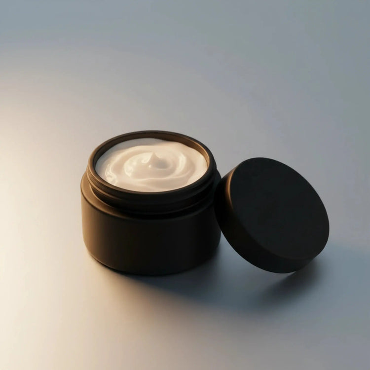 An open matte black cosmetic jar filled with white cream, with its matching lid leaning against it on a clean, light gray background.