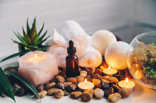 Bath bombs and three lit candles surrounded by river rocks, towels, and succulents in spa setting