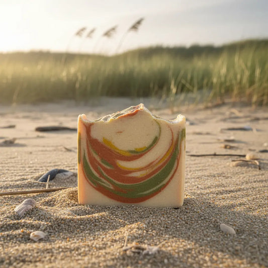 Unwrapped Dune Grass tallow soap bar nestled in the warm sand among wild dunes, its earthy green hue blending with the natural landscape.