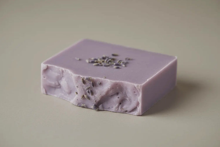 Purple soap bar with visible herbs on a beige background