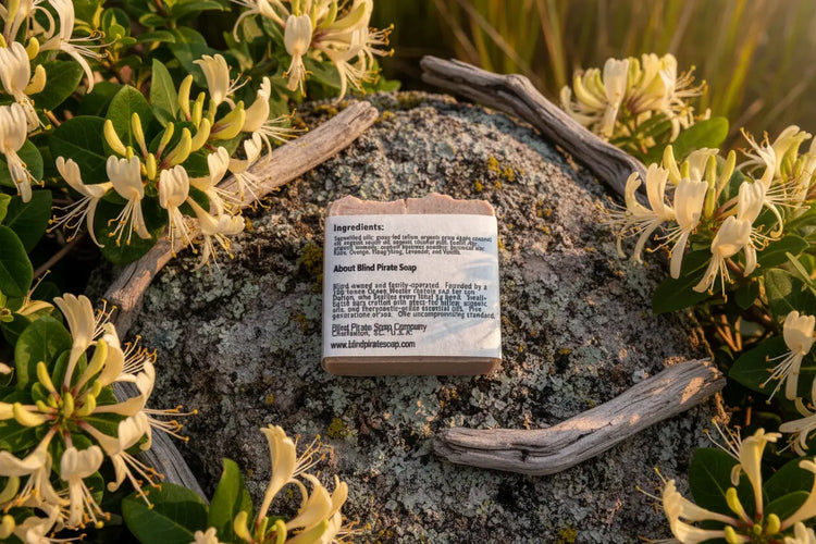 Honeysuckle — soap back label with ingredients list, surrounded by wild blooms on tabby stone, golden hour light