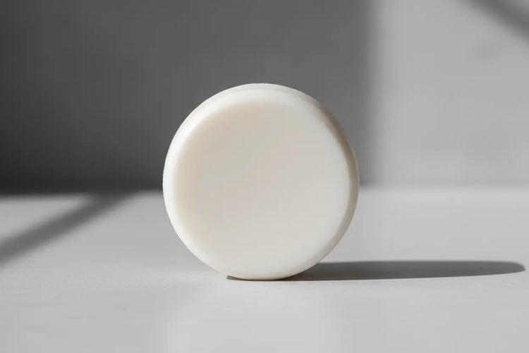 plain white round shampoo tallow bar unscented no added ingredients only 3 ingredients a beautiful white round shampoo bar stands on it's side in the light of a gentle sun.