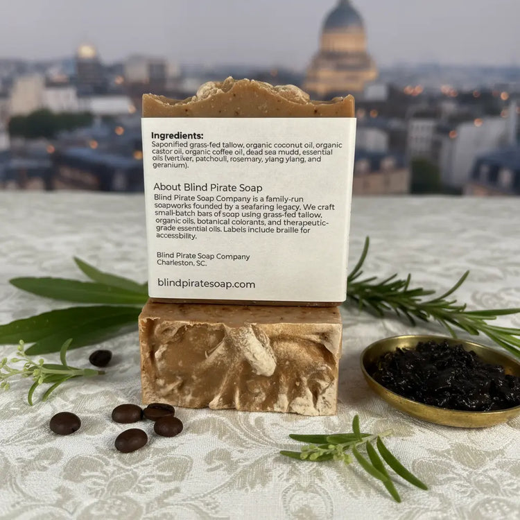 Back panel of Stone Ground tallow soap bar beside caviar and roasted coffee beans, golden Paris skyline glowing softly in the distance.