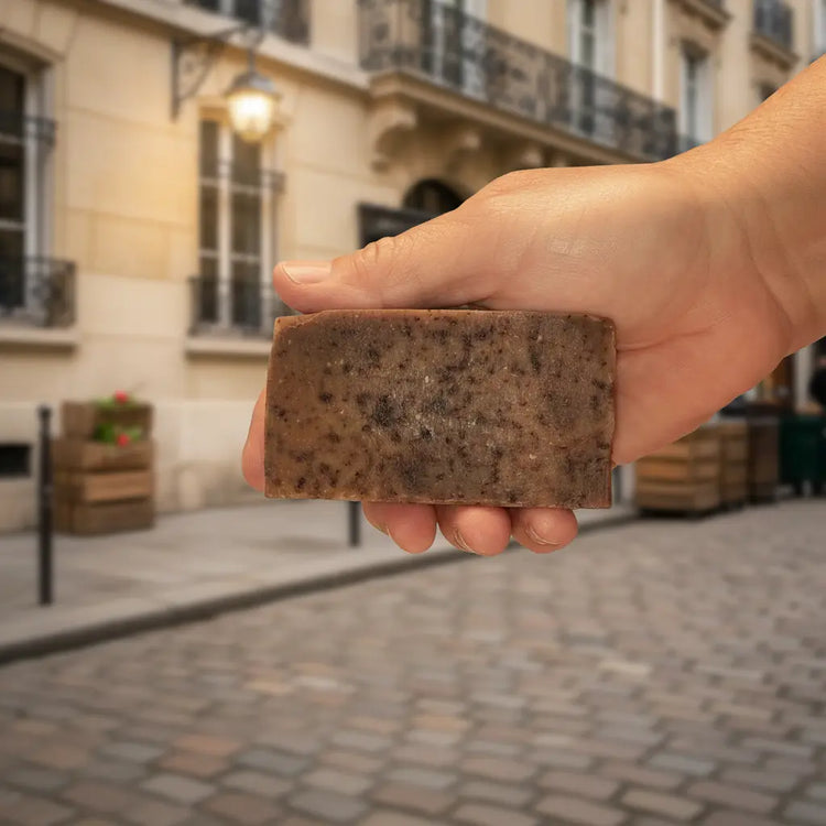Stone Ground natural soap bar with dark botanicals, set against a warm Parisian stone wall background.