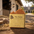 The Stable tallow soap bar on weathered wood, hay, horse in stable door, grand estate behind. Blind Pirate Soap Co.