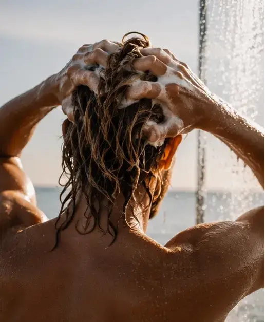 Lathering Sailor's Mead tallow shampoo bar into wet hair outdoors, rich foam, ocean in background