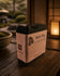 Black Flag tallow soap with Brailled paper label on warm wood surface, lantern glow in background.