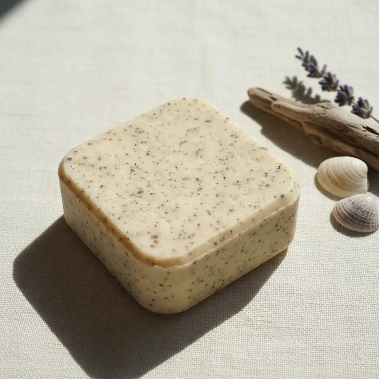 Salt & Timber Travel Size Handcrafted Organic Hair Care Shampoo Bar is laid on a towel with seashells, driftwood, and a beach flower