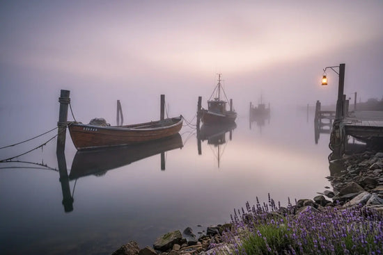 Misty dawn harbor, wooden boats moored in still purple water, lantern glowing on the dock. Blind Pirate Soap Co.
