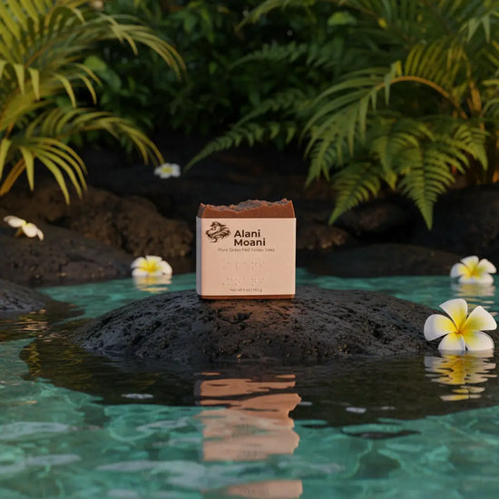 Alani Moani front panel rests on dark lava rock, lush tropical foliage and bright yellow Hawaiian flowers all around.
