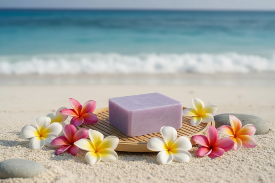 Alani Moani purple soap bar on bamboo tray with Hawaiian beach and ocean waves in background, plumeria flowers