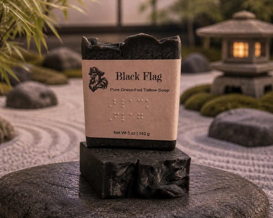 Black Flag tallow soap bars stacked in a Zen garden with raked gravel and stone lantern. Blind Pirate Soap Co.