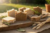 7 bars of handmade grass fed tallow soap lay on a weathered board in dappled sunlight
