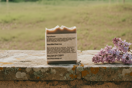 Blind Pirate Lilac soap back panel flat lay on warm limestone stone surface, dried lilac sprig, soft natural light

