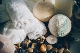 Two bath bombs on wet river rocks with tea light candle and fluffy white towels - perfect spa setting for tallow products