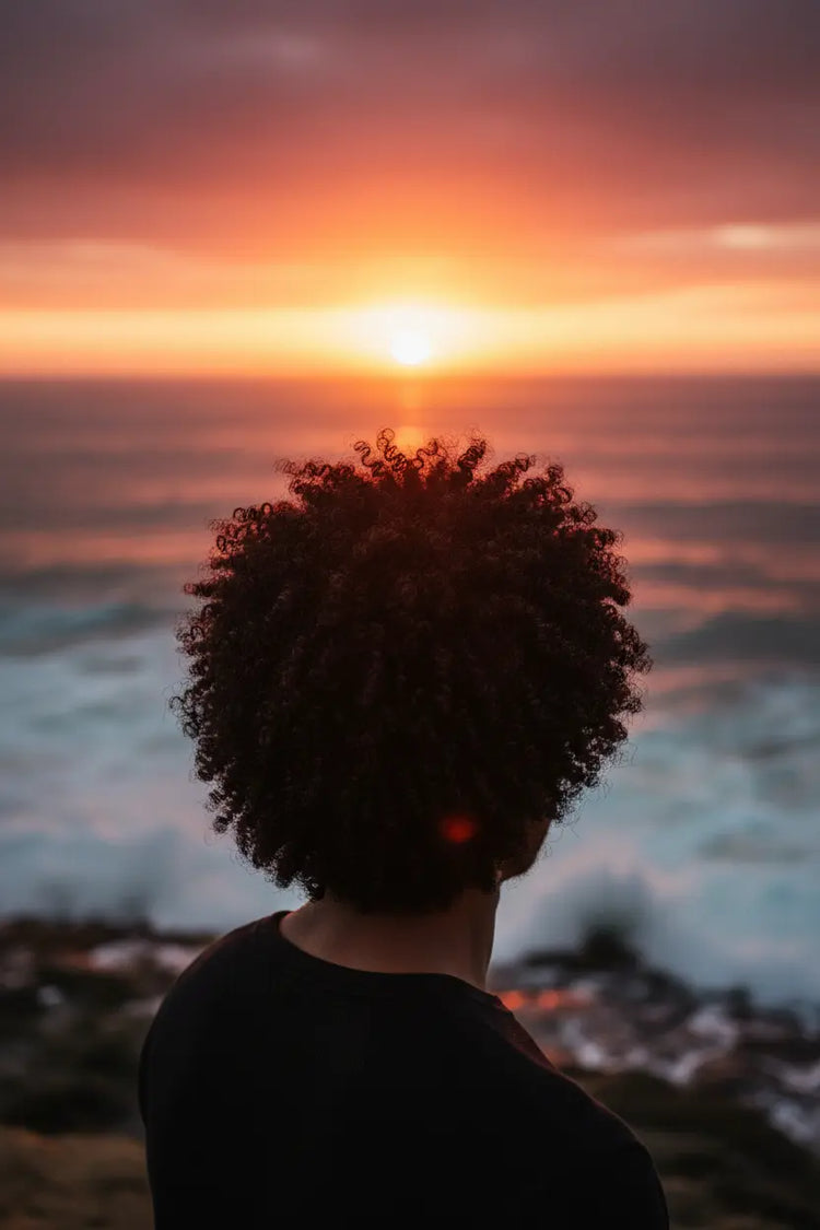 Natural Afro Male watching the sun fall behind the ocean horizon.  very healthy hair.