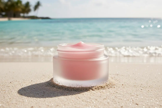 Ditch Kit rose tinted lip balm by Blind Pirate Soap Co resting on white sand with crystal clear Caribbean turquoise water in the background.