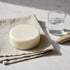 Still Water round ivory tallow bar on white marble with linen cloth and glass vessel — Blind Pirate Soap Co.