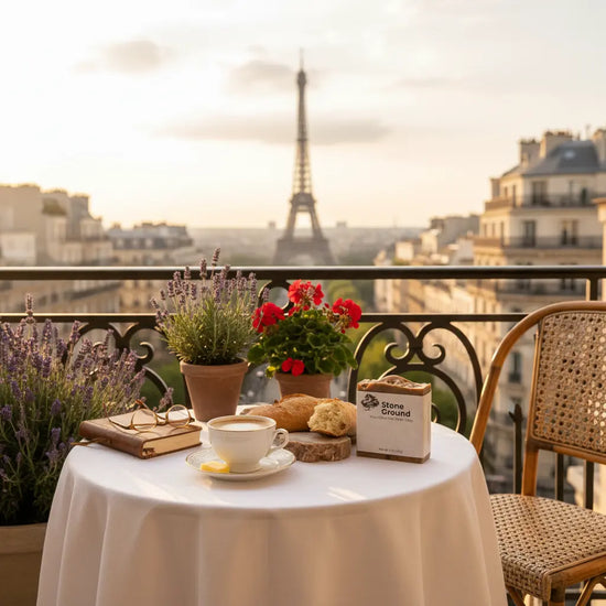 Stone Ground Parisian sunset moment, a linen-draped Paris balcony table with fresh lavender, croissants, coffee and a book, Eiffel Tower beyond.
