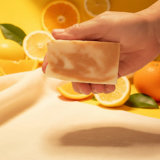 Hand holding a rustic-cut bar of Sunshine & Citrus tallow soap, showing warm golden turmeric swirls against pale kaolin clay layers — Blind Pirate Soap Co.